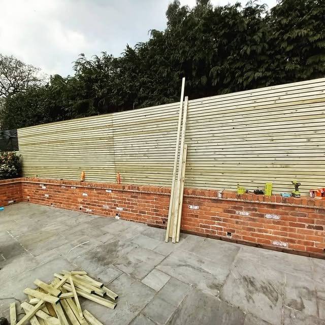 New fence panels being installed alongside a brick wall